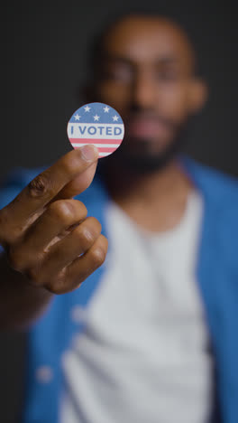 Vertical-Video-Portrait-Of-Shot-Of-Man-Holding-I-Voted-Sticker-In-American-Election-With-Pull-Focus